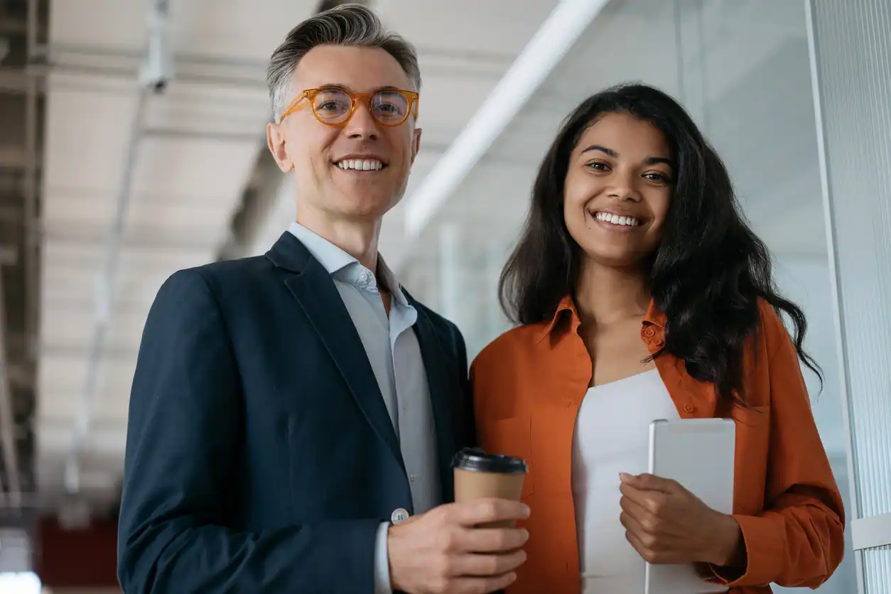 Colleagues standing together holding digital tablet and cup of coffee in modern office